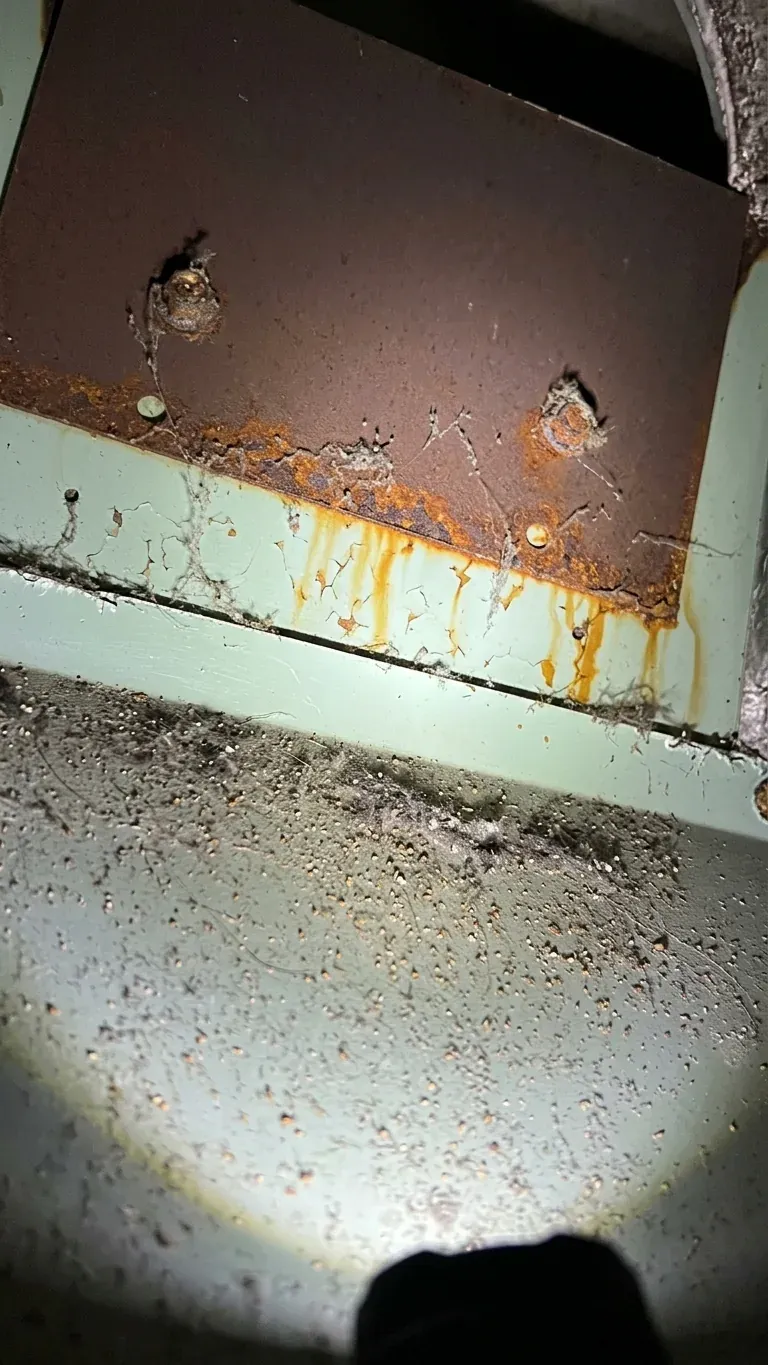Rusted draft diverter panel inside an old furnace cabinet, with rust streaks running down